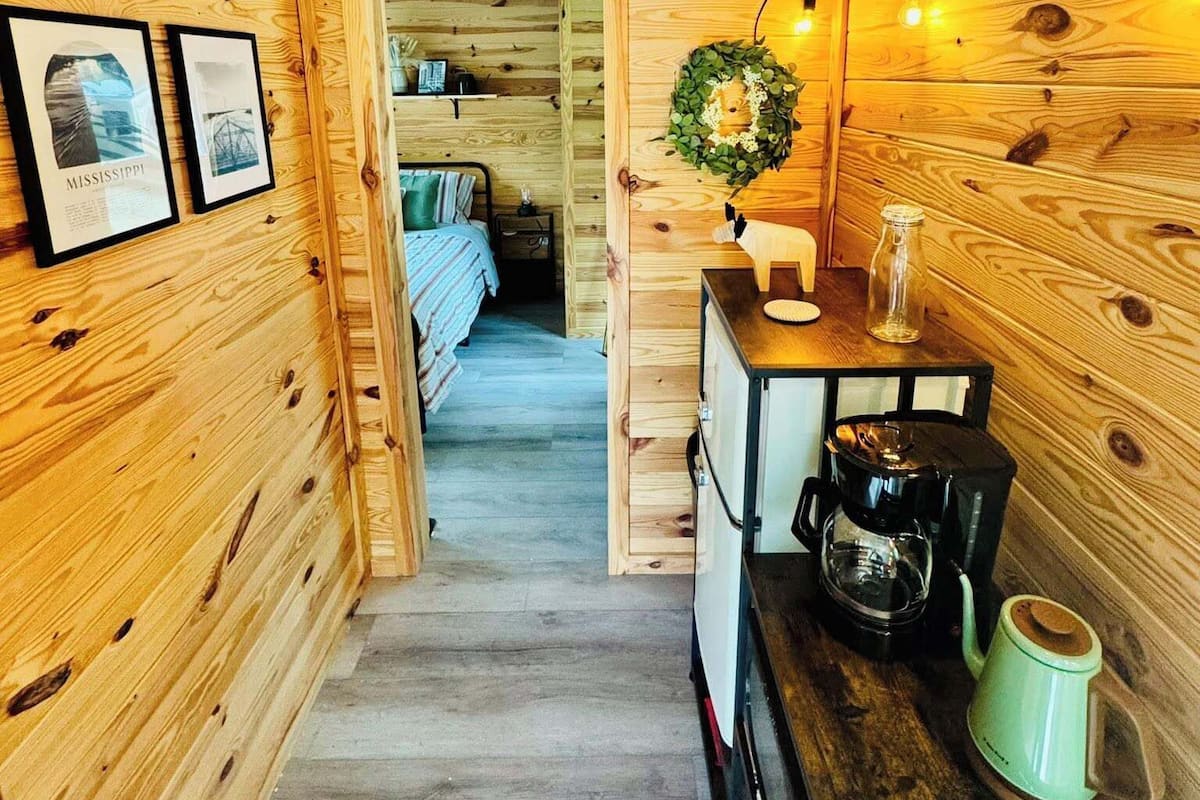 A wooden interior with a bed, a coffee station, and framed pictures on the wall.