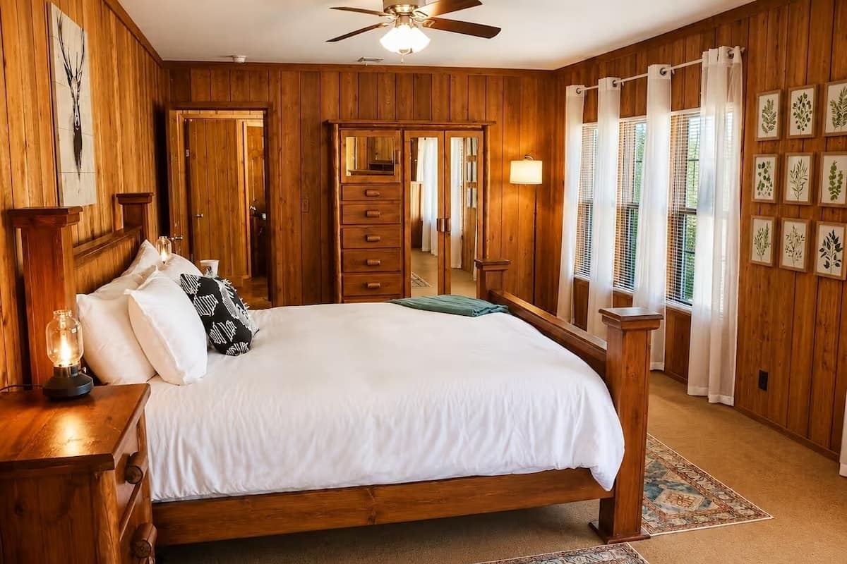 A wooden-paneled bedroom with a bed, nightstands, a ceiling fan, and a large mirror.