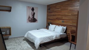 A bedroom with a bed, a chair, a nightstand, a wall-mounted artwork, and a wooden accent wall.