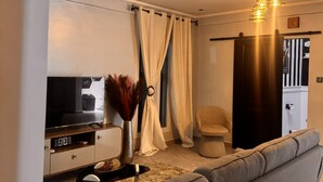 A modern living room with a grey sofa, a flat-screen TV, a decorative vase, and a wooden cabinet.
