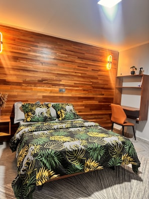 A bedroom with a wooden headboard, a bed with a leaf-patterned bedspread, a nightstand, a chair, and a shelf with items.
