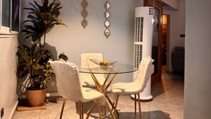 A dining area with a glass table, white chairs, and a potted plant.