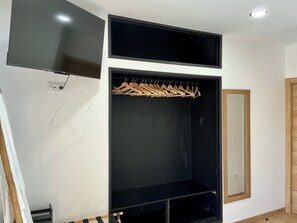 Ein Zimmer mit einem schwarzen Kleiderschrank, einem Spiegel und einem an der Wand befestigten Fernseher.