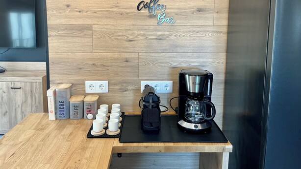 Una cocina con una barra de café, una cafetera y recipientes para azúcar y leche en la encimera.