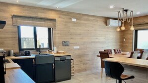 Una cocina moderna con lavavajillas, una zona de comedor con mesa y sillas, y un ventanal que proporciona luz natural.