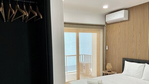 Habitación de hotel con cama, pared de paneles de madera, unidad de aire acondicionado y vista a través de un ventanal.