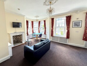 Ein Wohnzimmer mit Kamin, Fernseher, einer Kristallleuchtre, einem Sofa und einem Essbereich mit Tisch und Stühlen.