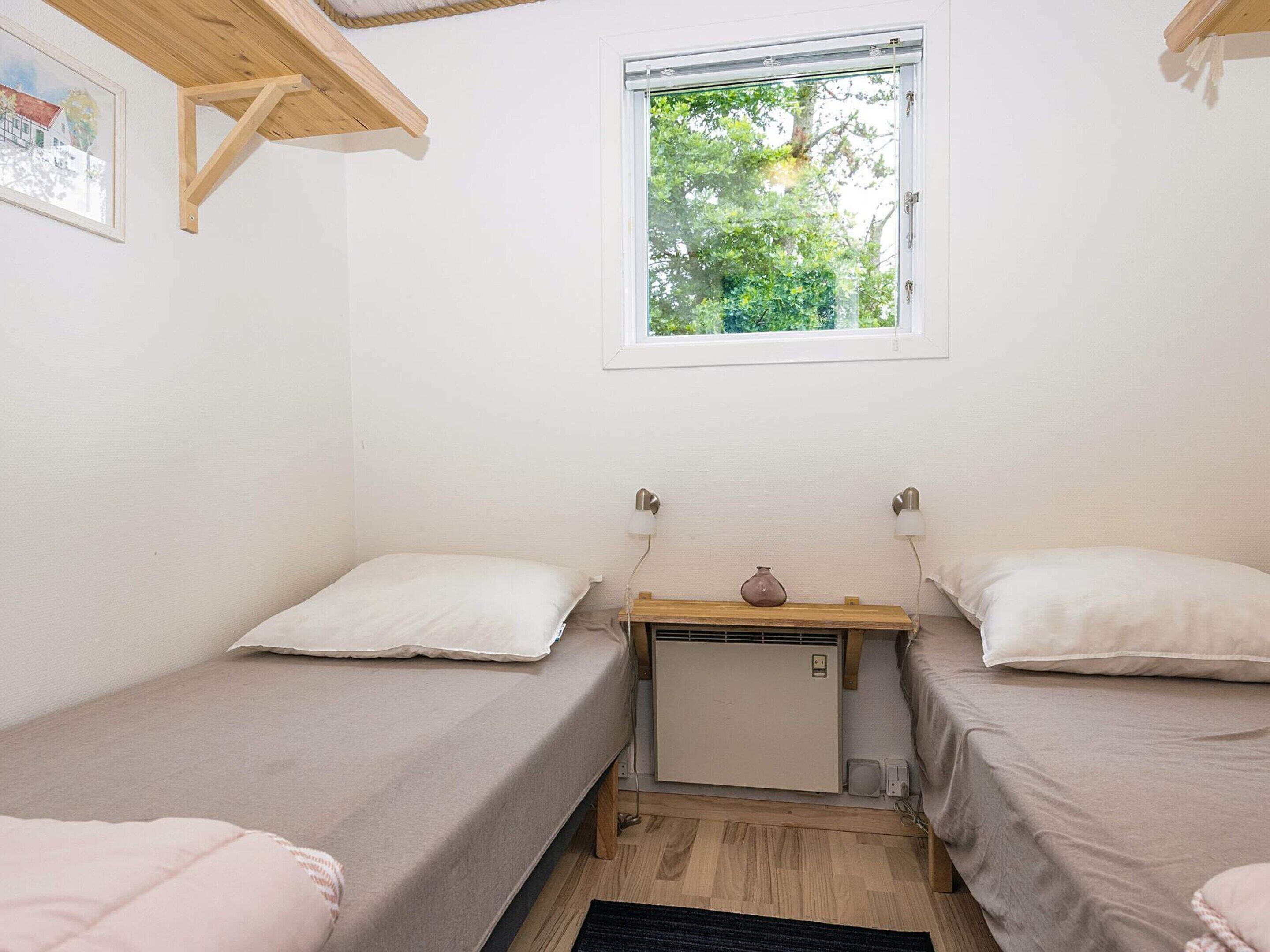 Eine kleine, einfache Unterkunft mit zwei Einzelbetten, einem Tisch mit einer Vase und einem Fenster mit Blick auf Grünflächen.