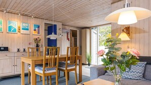 Una habitación acogedora con techo de madera, una mesa de comedor con sillas, un sofá, un florero con flores y una lámpara.