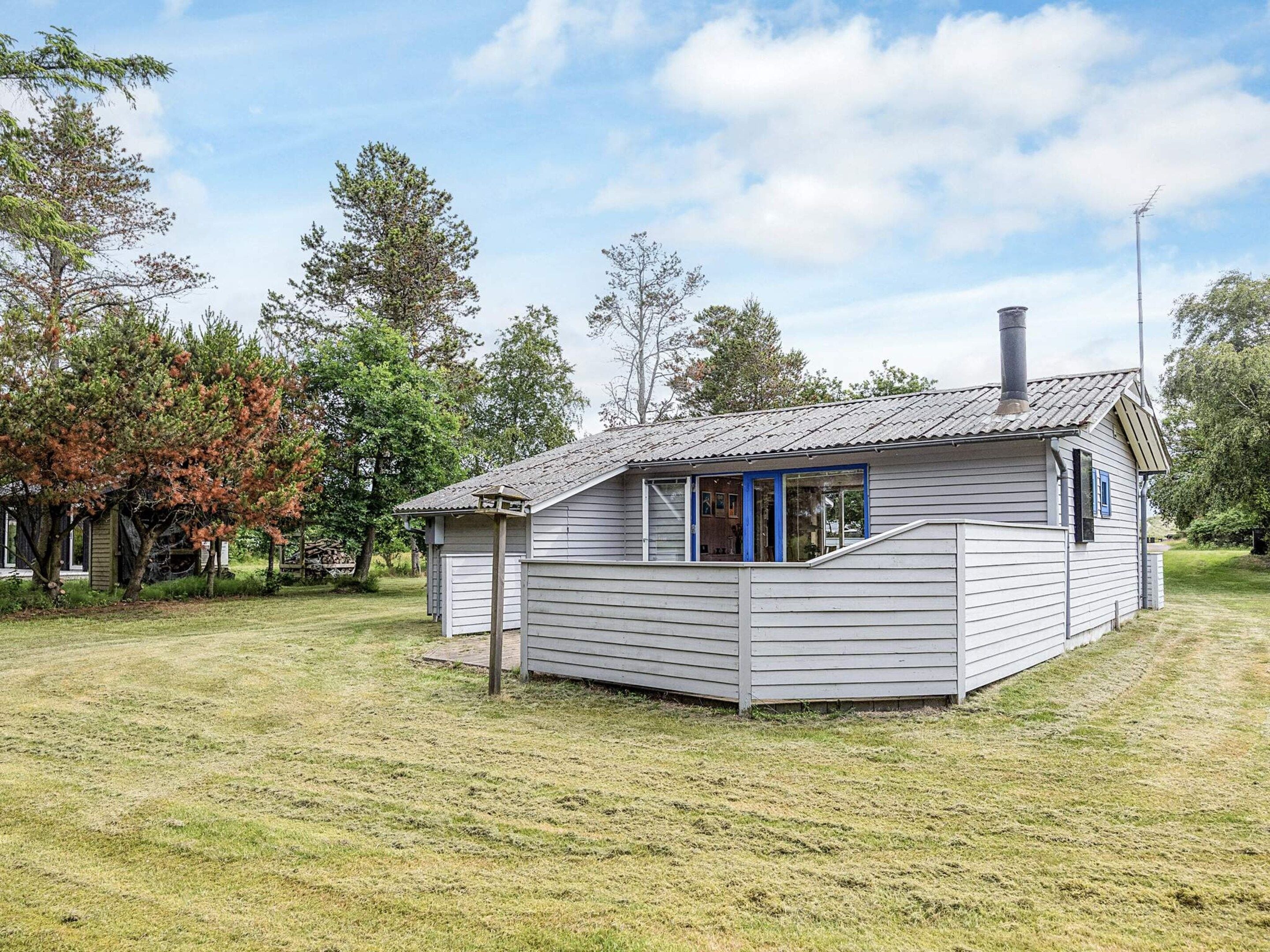 A small, single-story cabin with a sloped roof and a chimney, surrounded by a grassy area and trees.