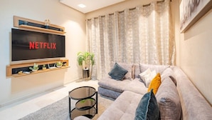 A living room with a large flat-screen TV, a sofa, a coffee table, and a potted plant. - Studio - Golf & Pool view- Cadre chic et paisible (Marrakesh)