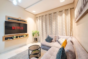 Ein Wohnzimmer mit großem Flachbildfernseher, einer Couch, einem Couchtisch und einer Topfpflanze.