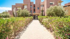 A modern building with a central entrance, surrounded by well-maintained gardens and a paved pathway. - Studio - Golf & Pool view- Cadre chic et paisible (Marrakesh)
