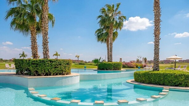 A swimming pool with palm trees, lounge chairs, and a clear sky. - Studio - Golf & Pool view- Cadre chic et paisible (Marrakesh)