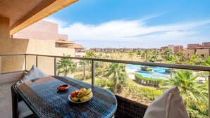 A balcony with a table, a bowl of fruit, and a view of a pool and buildings. - Studio - Golf & Pool view- Cadre chic et paisible (Marrakesh)