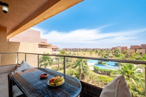 Ein Balkon mit Tisch, Obstschale und Blick auf Pool und Gebäude.