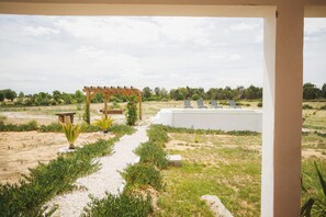 A garden with a pergola, a pathway, and a white wall with lounge chairs.