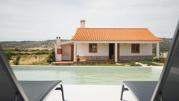 A house with a swimming pool, two lounge chairs, and a view of the countryside.