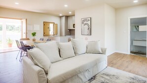 A living room with a sofa, a dining table, chairs, a kitchen area, and a sliding door leading to a bathroom.