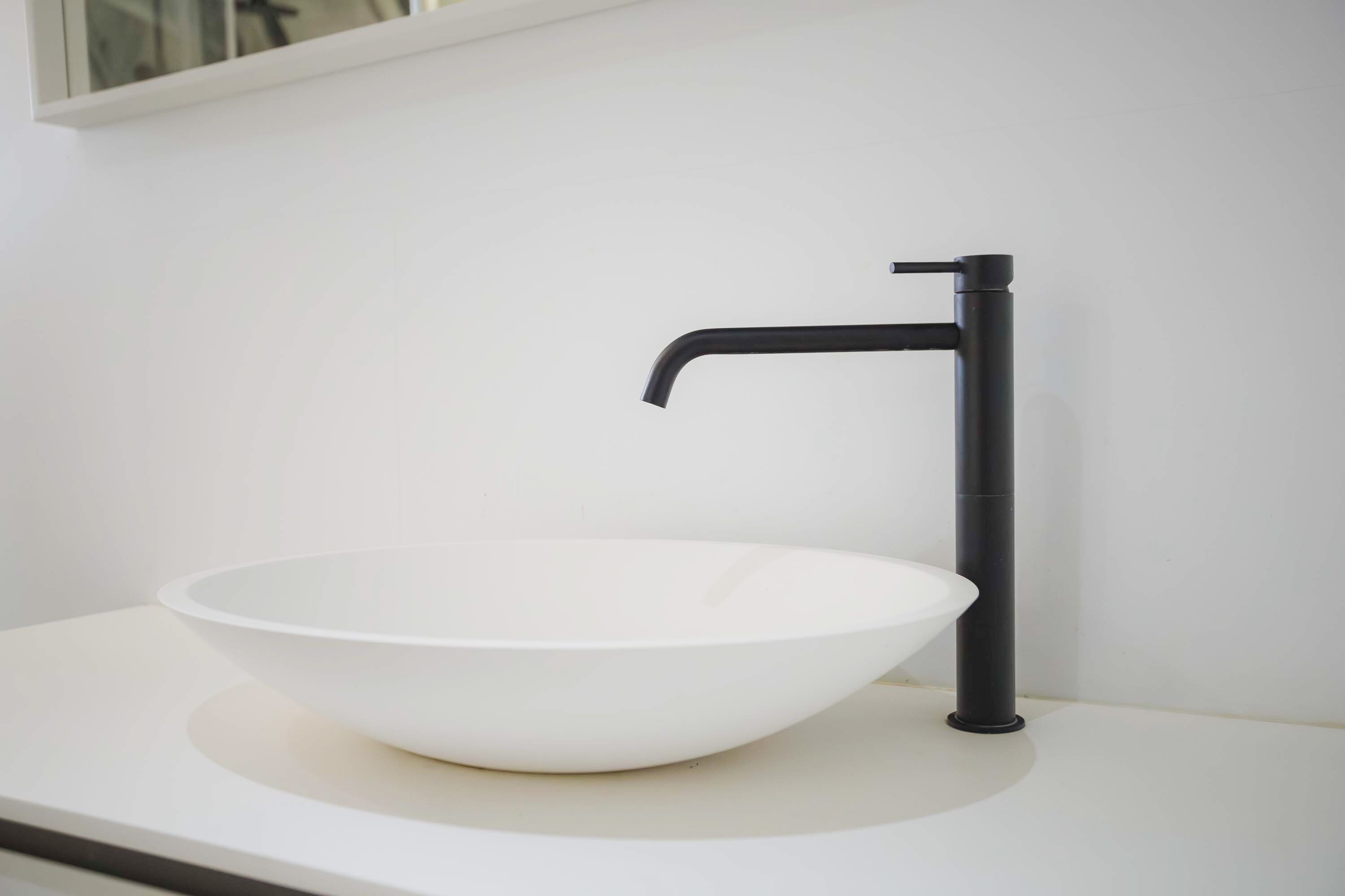 Ein weißes Waschbecken mit einem schwarzen Wasserhahn auf einer weißen Arbeitsplatte.