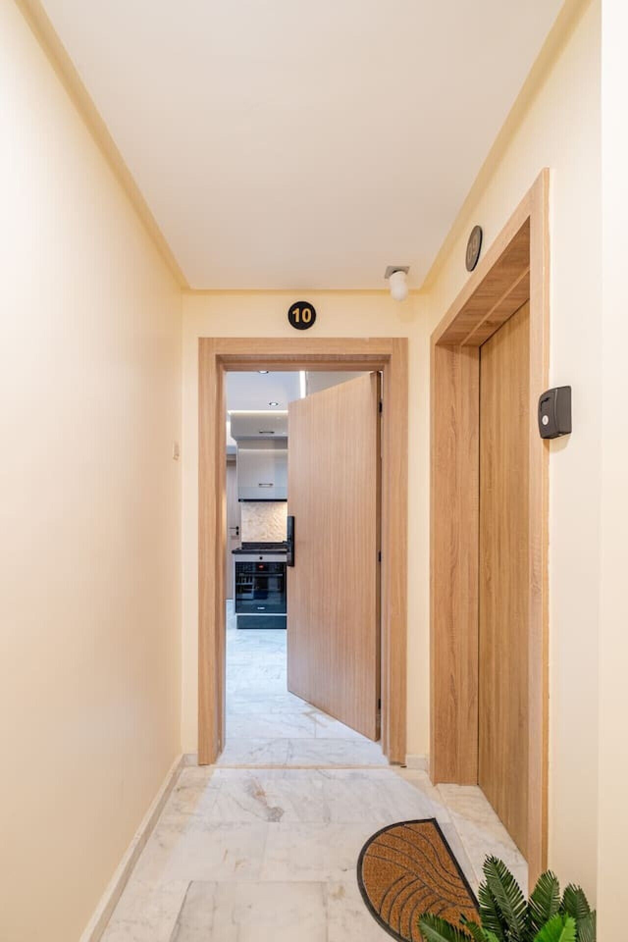 Un pasillo con una puerta de madera marcada '10', que da a una habitación con zona de cocina.
