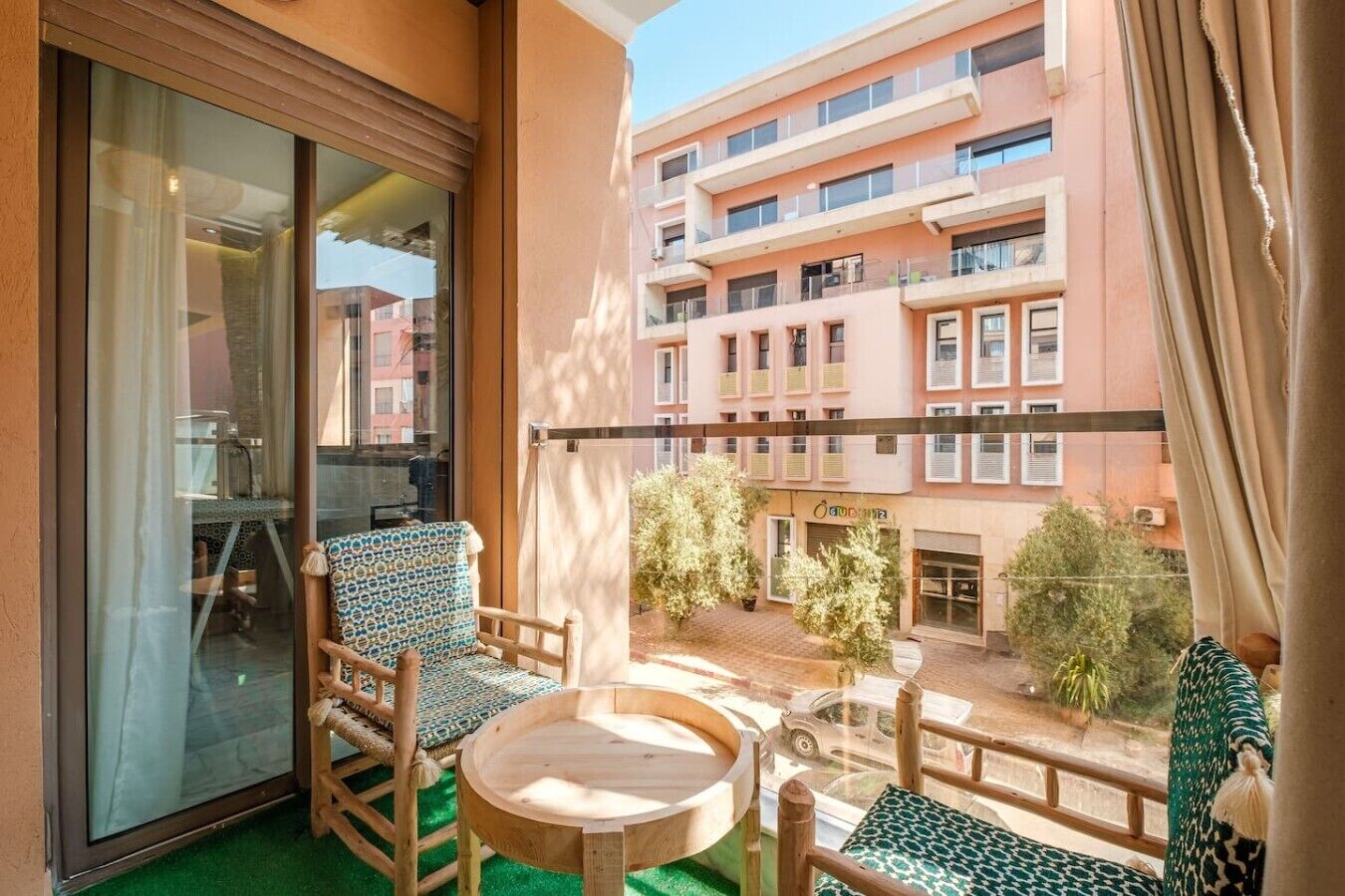 Un balcon doté d’une porte vitrée, de deux chaises, d’une petite table ronde et offrant une vue sur un immeuble à plusieurs étages, lui aussi doté de balcons.