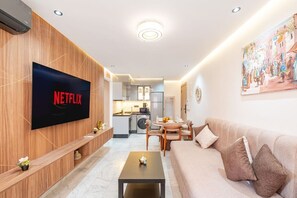 A modern living room with a flat-screen TV, wooden paneling, a sofa, a dining area, and a kitchen in the background. - Guéliz Centre-King Bed- 5 min a pied de Carré Eden (Marrakesh)