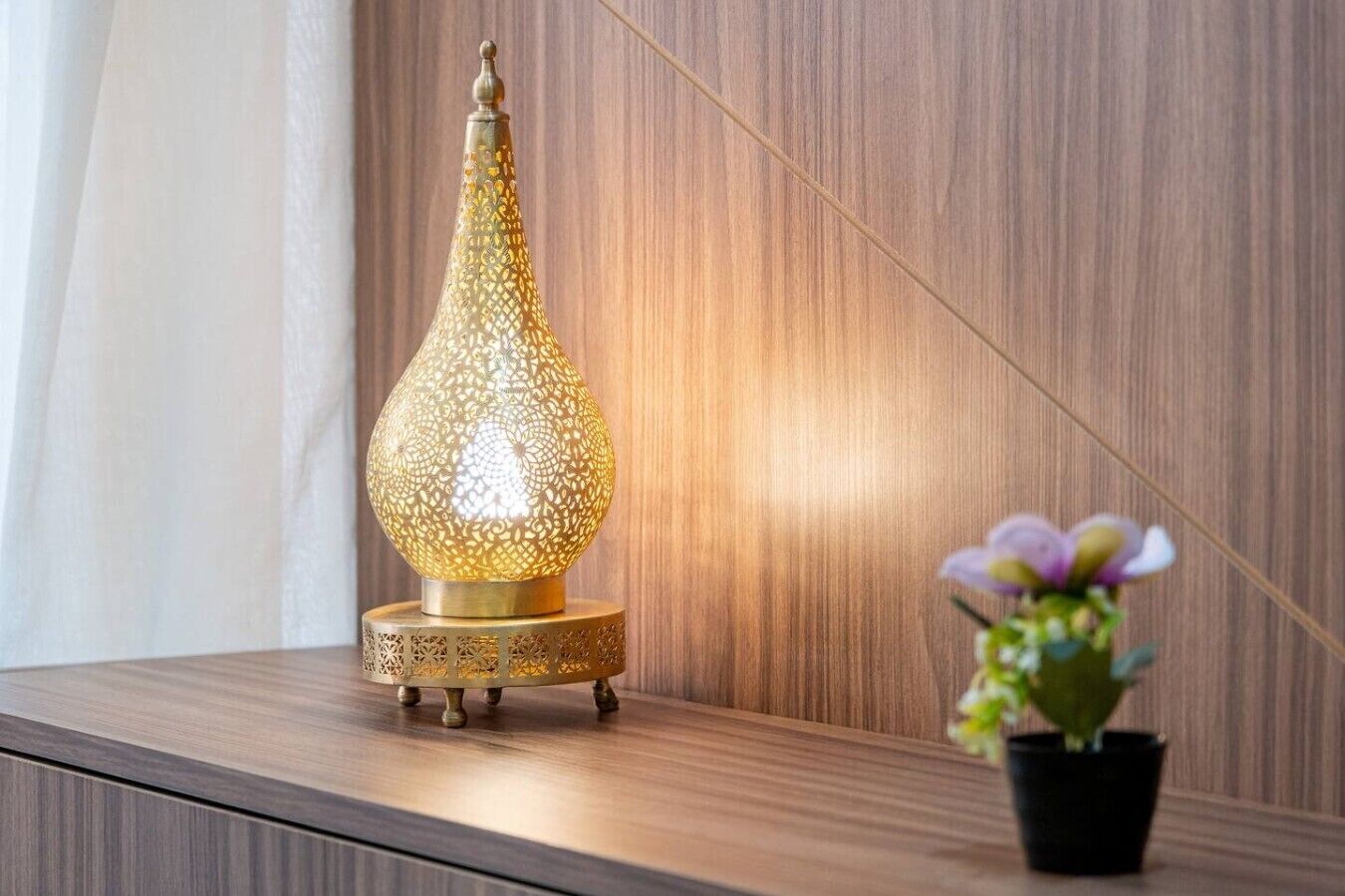 A decorative lamp with intricate patterns on a wooden surface, accompanied by a potted plant.