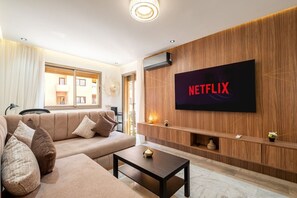 Ein modernes Wohnzimmer mit einer Couch, einem Couchtisch und einem an der Wand befestigten Fernseher, der das Netflix-Logo zeigt.
