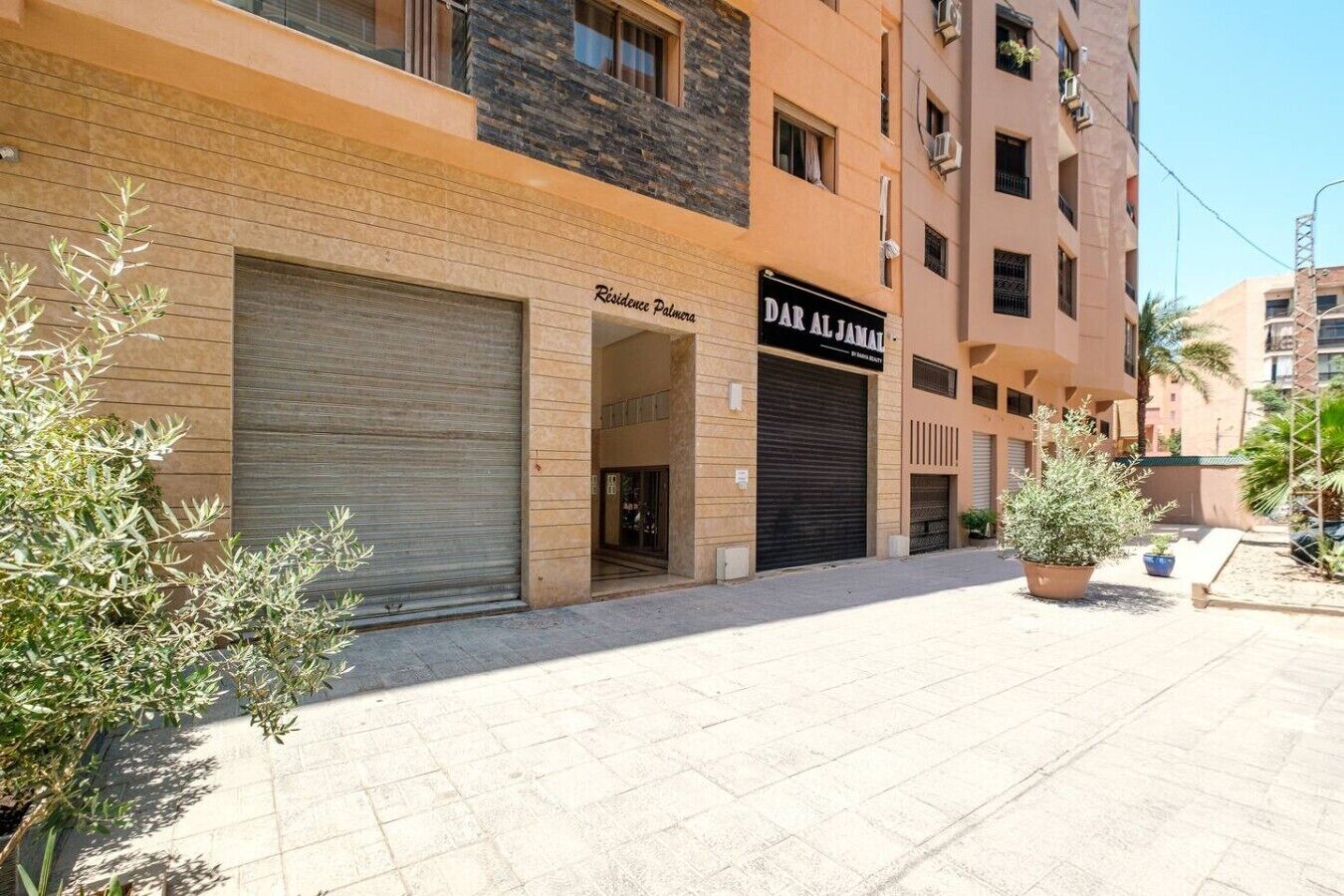 A building with a closed garage door, a sign for 'Dar Al Jannah,' and a potted plant in the foreground.