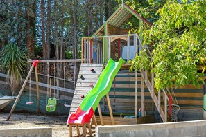 Ein Spielplatz mit Rutsche, Schaukeln und einer kleinen Holzkonstruktion.