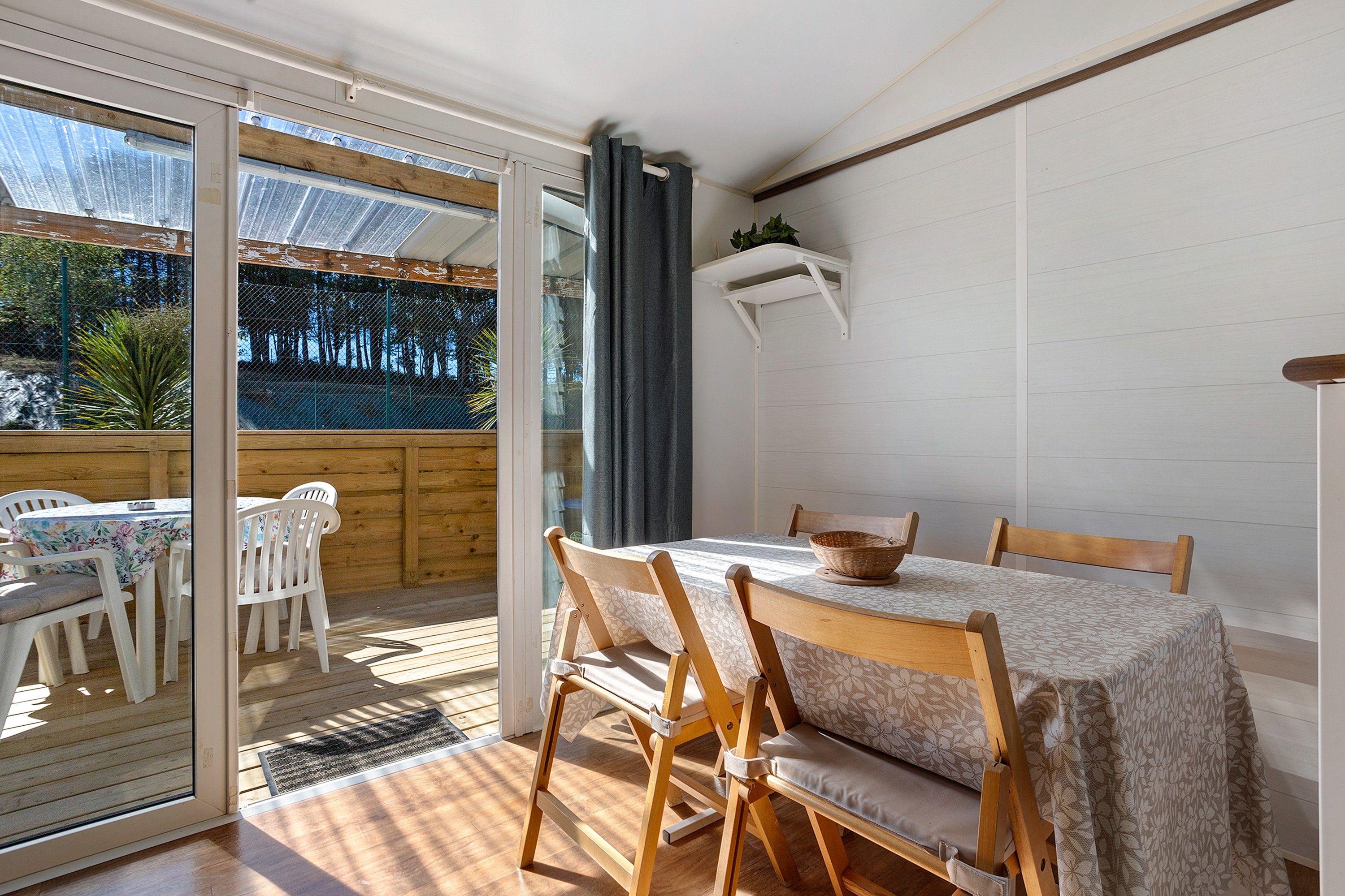 A dining area with a table and chairs, a sliding glass door leading to an outdoor space, and a small shelf with a plant.