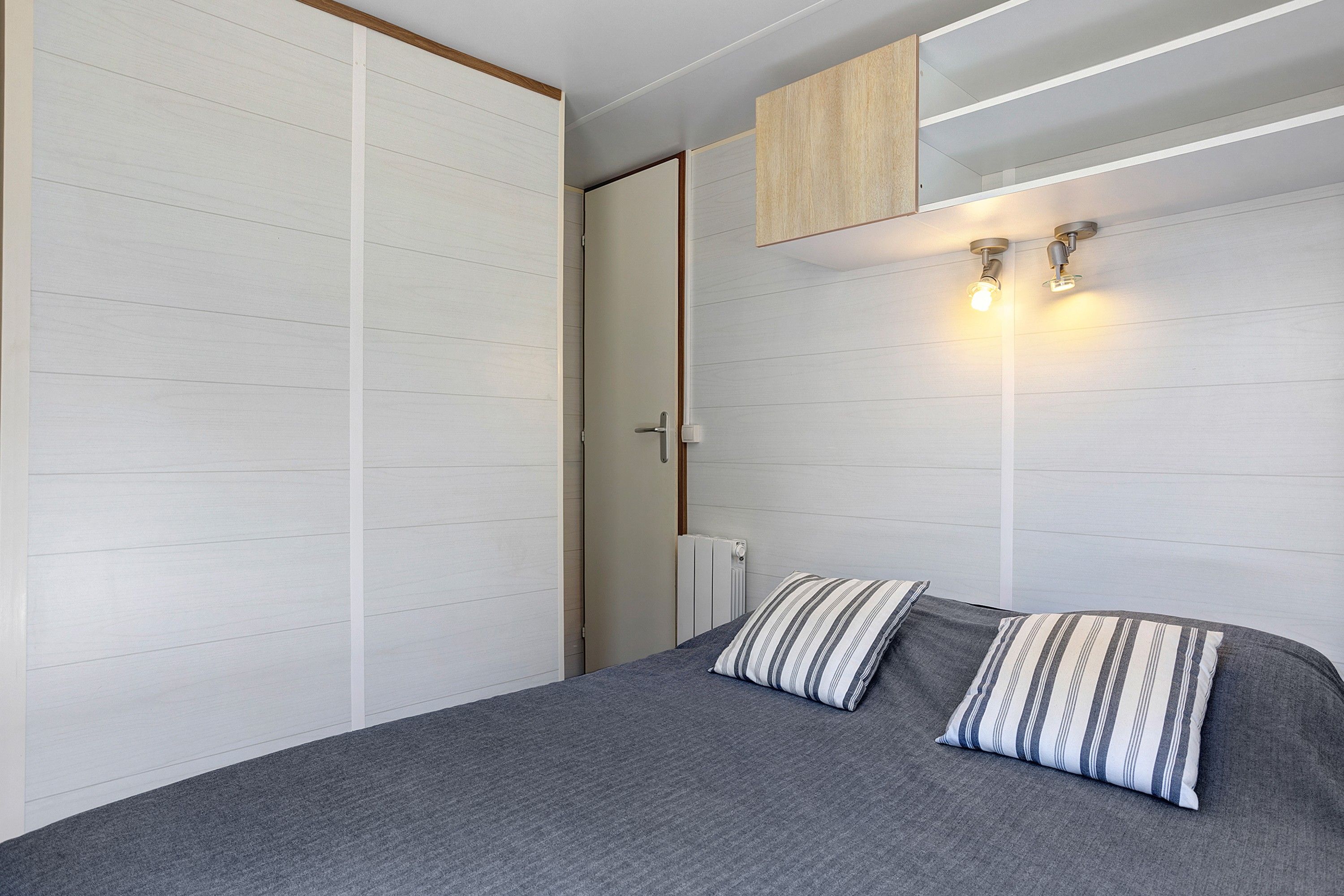 A bedroom with a bed, two pillows, a wardrobe, a radiator, and a mirror.