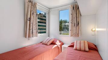 A room with two single beds, each with a striped pillow, and a window with curtains.
