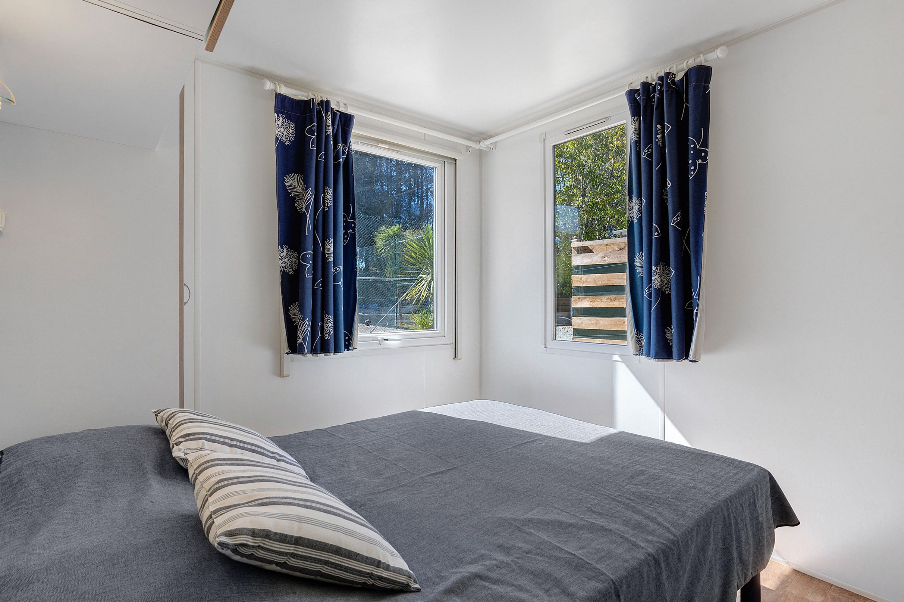 Een slaapkamer met een bed, een kussen en twee ramen met gordijnen.