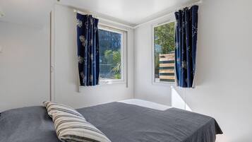 Un dormitorio con una cama, un almohadón y dos ventanas con cortinas.