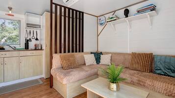 A modern living space with a sofa, a small table, a potted plant, and a kitchen area with utensils.