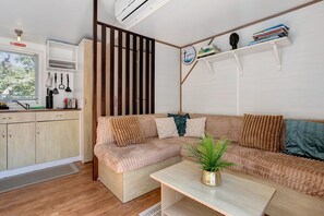 Ein stilvoller Wohnraum mit Sofa, einem kleinen Tisch, einer Topfpflanze und einer Küchenzeile mit Kochgeschirr.