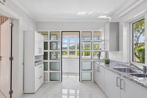 Eine moderne Küche mit weißen Schränken, einer Arbeitsplatte aus Granit und einem großen Fenster mit Blick ins Grüne.