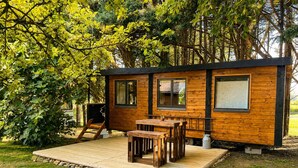 A wooden cabin with a deck, a table, and chairs.
