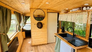 A compact wooden cabin with a kitchenette, a bed, and a window with curtains.