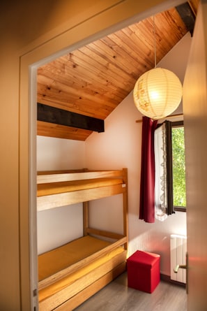 A room with a wooden bunk bed, a red ottoman, a hanging light fixture, and a window with curtains. - Le Petit Nid Family Chalet in Corrençon-en-Vercors, near the slopes and village (Corrençon-en-Vercors)