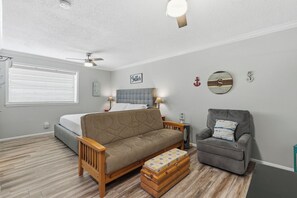 A bedroom with a bed, a sofa, a chair, a small table, and a ceiling fan.