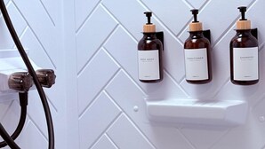 Un bagno con una parete bianca a motivo a spina di pesce, tre flaconi di bagnoschiuma, balsamo e shampoo, e un soffione.