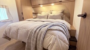 Una camera da letto con un letto, una finestra con tende e armadietti a muro in legno.