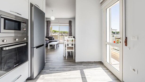 Una cocina moderna con electrodomésticos integrados, un comedor con mesa y sillas, y vistas a través de un ventanal.