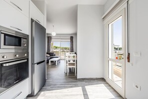 A modern kitchen with built-in appliances, a dining area with a table and chairs, and a view through a glass door. - Spacious Apartment Near the Beach | Gjiri i Lalzit by PikHost (Gjiri i Lalzit)