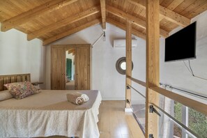 Ein Schlafzimmer mit Holzbalkendecke, einem Bett mit gemustertem Überwurf, einem Fenster mit Vorhang und einem angebrachten Fernseher.