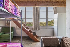 Ein Zimmer mit Etagenbetten, einer Treppe, einem grünen Stuhl, einem Bett mit Quiltdecke und Blick auf Hügel durch ein Fenster.