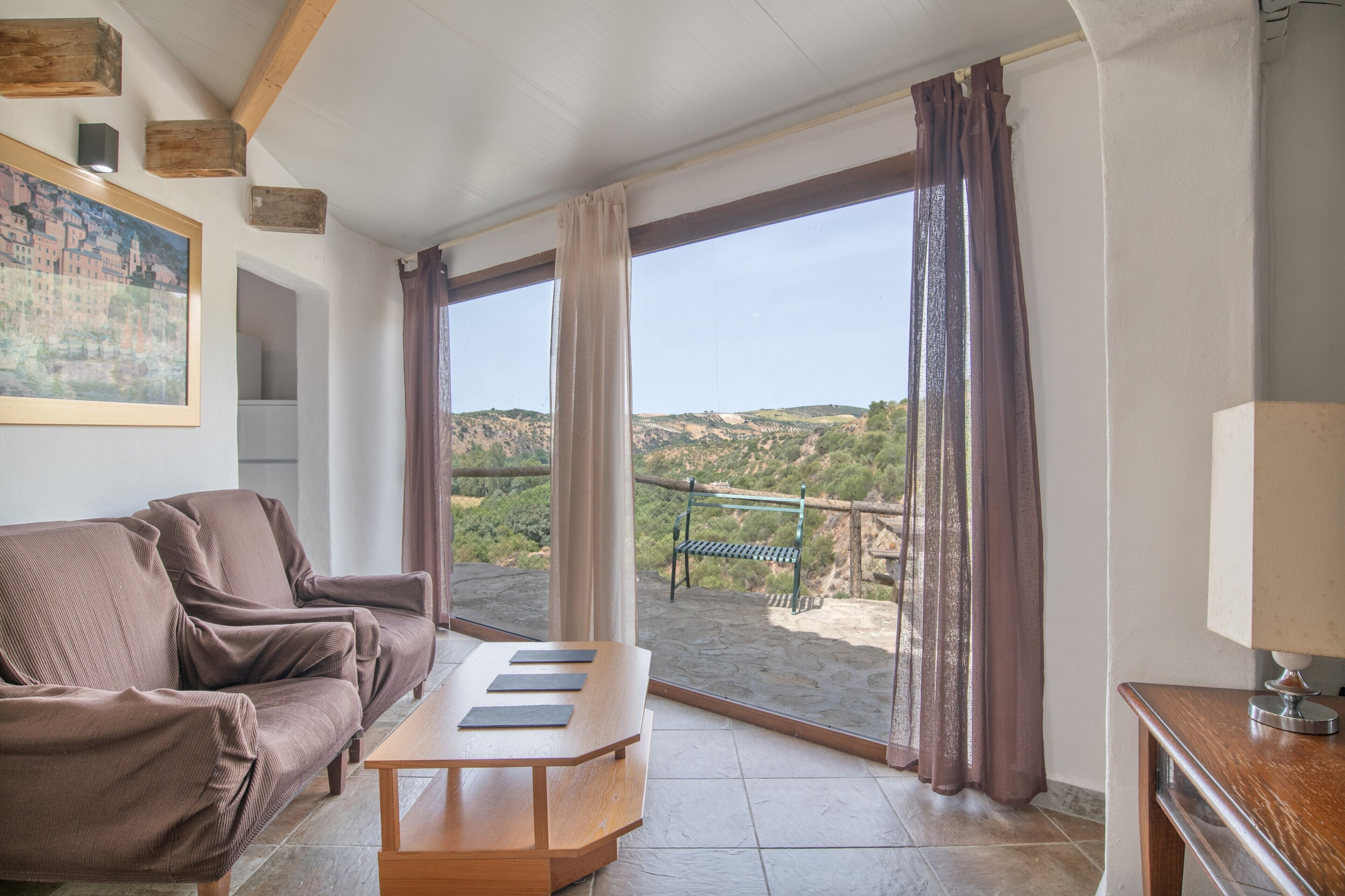 Una habitación con sofá, una mesa de madera y vistas a una ladera a través de amplios ventanales.